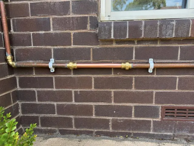 Copper water pipe repaired on an exterior brick wall beneath a window in Berala