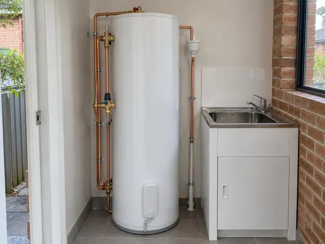 White hot water cylinder beside a laundry sink and brick wall in a tiled utility room in Newington