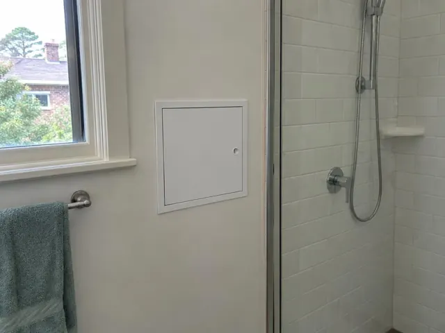 Bathroom wall with a small access panel beside a shower and window in Auburn